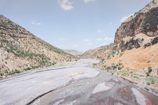 A mountain river flows in a valley of the Tien Shan Mountains in Tajikistan in the Pamirs. A noisy mountain river flows between rocky mountain slopes in the summer during hot weather