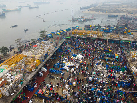 Aerial view of a bustling fish market with numerous people, colorful crates, and boats docked along the river in Chattogram, Chittagong Division, Bangladesh.