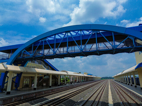 Aerial view of Soydabad Railway Station featuring a prominent blue pedestrian bridge spanning over the railway tracks under a bright blue sky in Sirajganj, Rajshahi Division, Bangladesh.