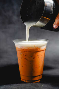 Close-up of pouring milk into a glass of Thai milk tea with ice.
