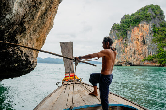 Boatman navigating longtail boat past karst cliffs in thailand
