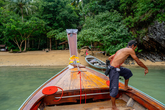 Local boatman navigating longtail boat towards tropical beach
