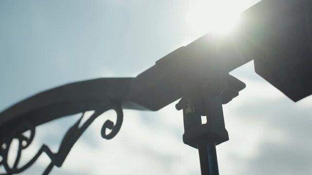 Close up of metal bracket and support structure with intricate scrollwork showing detailed hardware components. Sunlight creates lens flare against clear sky background. Soft lighting