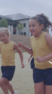 Animation of sports icons over happy diverse schoolgirls playing football on sports field
