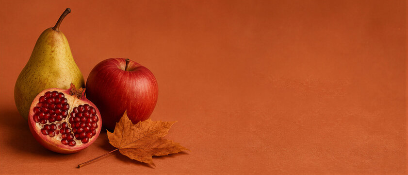 Autumn harvest still life with pear apple pomegranate and dry maple leaf on terracotta background. Mabon equinox celebration abundance and gratitude concept. Banner with copy space