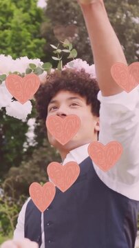 Animation of pink hearts over happy diverse couple dancing in garden on wedding day