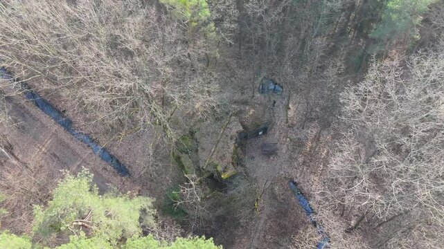 An aerial pan right and tracking shot over a lush forest in Rhineland-Palatinate, Germany. Streams wind through the hilly terrain, revealing an overgrown concrete bunker.