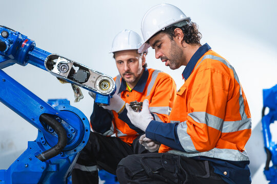 Robotics engineers repairing and inspecting industrial robot arm part in factory plant, Automation technicians working together on robotic machinery maintenance in facility