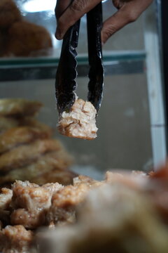 A close-up shot of a food vendor using tongs to pick up steamed siomay at a traditional Asian street food stall.