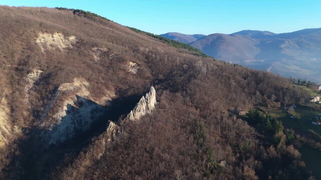 An aerial perspective of the unique Salti del Diavolo rock spires emerging from a forested mountain slope in Italy. Suitable for travel, geology, and nature documentaries.