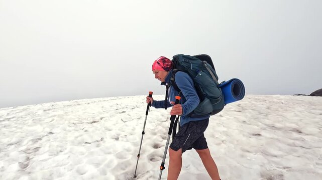 Tourist walks across snowfield, side view with trekking poles, boots and camping pack in Svaneti, Georgia, presenting seasonal route adaptation, gear performance and highland travel preparation