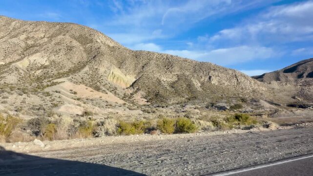 Arid Precordillera slopes rise beside Ruta Nacional 149 between Pachaco and Calingasta, with eroded ridges, alluvial ground and sparse xerophytic vegetation in San Juan, Argentina, moving car shot.