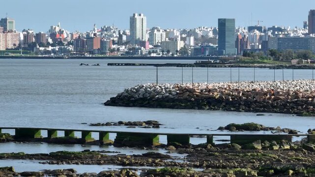 Montevideo rocky shoreline with concrete pier structures as the camera ascends to reveal the distant city skyline