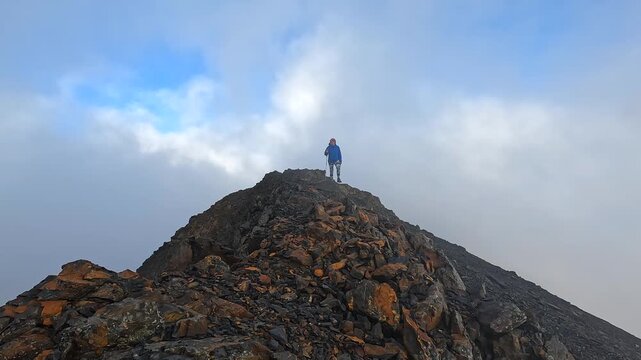 Solo hiker surveys rocky summit, low wide view, from a remote ridge in Svaneti, Georgia, supporting route scouting, wilderness navigation, mountaineering achievement, high-altitude tourism campaigns