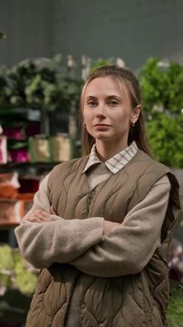 Vertical portrait of young adult Caucasian woman standing with arms crossed in wholesale flower warehouse. Footage is ideal for promoting floristry businesses or small business entrepreneurship