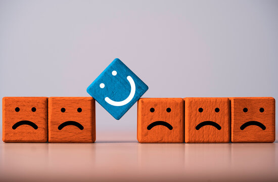 Positive attitude and optimism concept with a happy blue face standing out among sad orange faces symbolizing happiness, resilience leadership, individuality and positive mindset.