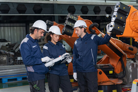 Engineers wearing hardhats using laptop computer to inspect and program robotic arm system in factory.
