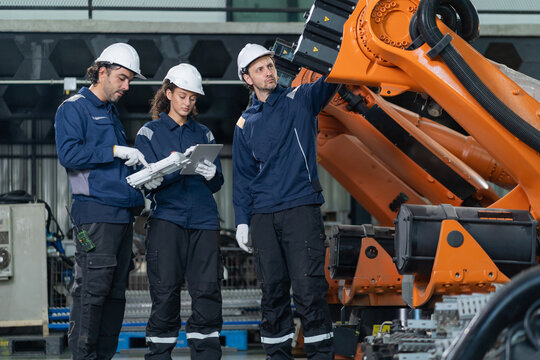 Engineers wearing hardhats using laptop computer to inspect and program robotic arm system in factory.