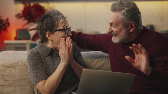 Excited married couple in their 50s read great news on laptop, lottery win