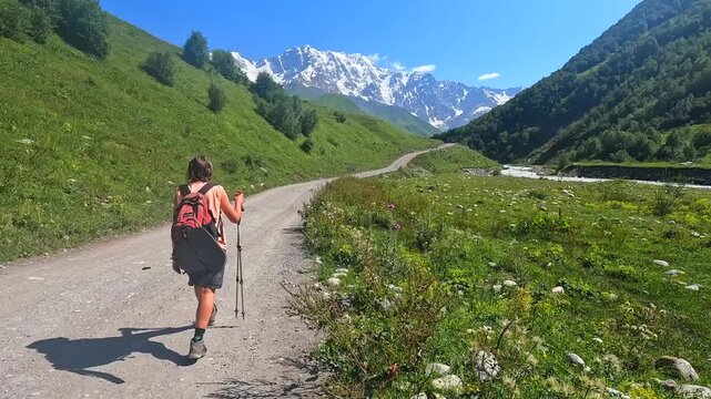 Hiker trekking in rear view along mountain road near Ushguli, Svaneti, Georgia, travel footage for hiking tours, adventure promotion, alpine route marketing, destination branding, tourism campaigns