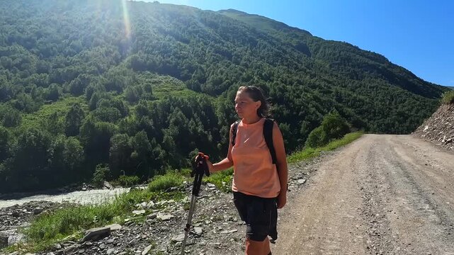 Female hiker trekking in medium shot on mountain road in Ushguli, Svaneti, Georgia, travel footage for guided hiking tours, outdoor training promotion, backpacking services, and active vacation ads