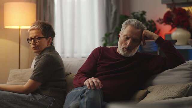 Upset middle-aged man and wife sit apart on sofa, serious relationship crisis