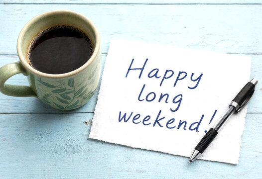 Handwritten happy long weekend greeting note with coffee cup and pen on wooden table