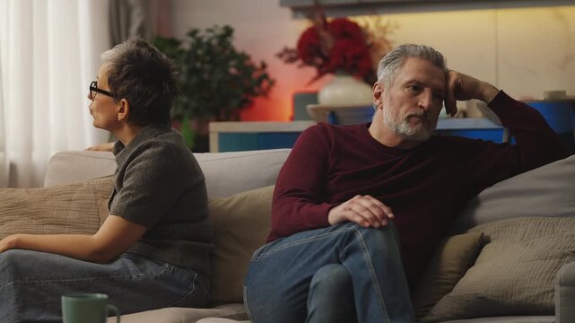 Sad middle-aged couple sit apart on sofa after fight, relationship problems