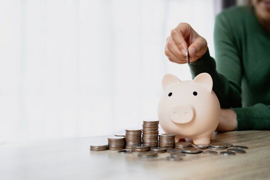 Woman putting a coin into a piggy bank surrounded by stacked coins. Symbolizing personal savings, financial planning, budgeting and future goals.