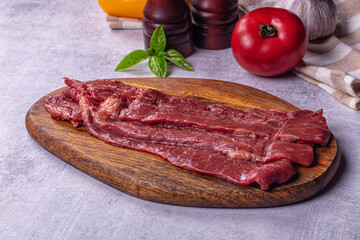 Obraz premium Raw beef steak slices on wooden cutting board with tomato basil and pepper mills