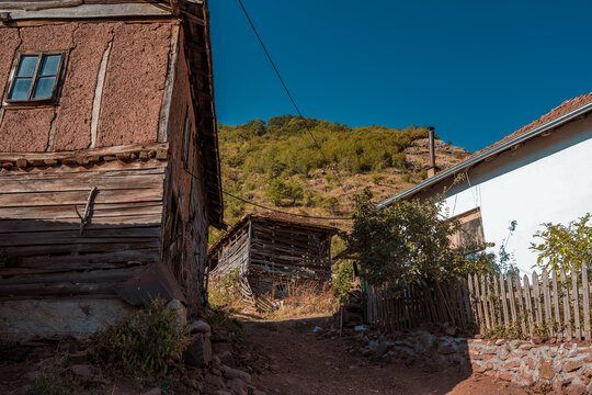 Narrow dirt path leading between traditional old mud and wooden houses toward green mountain hills in Topli Do village, Stara Planina nature reserve in Serbia.