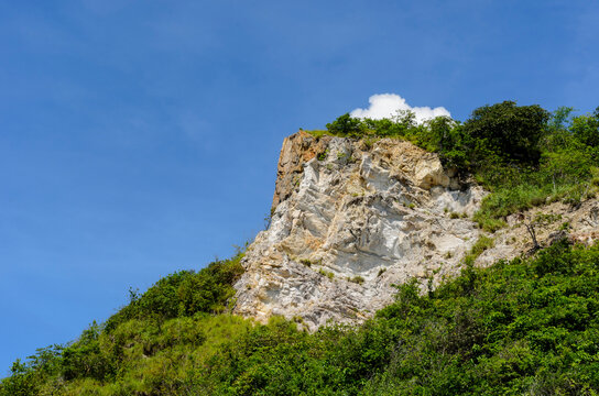 A landscape view of the rocky cliff of Samae San Island with some plants and a small cloud on a clear summer day. Shot from below
