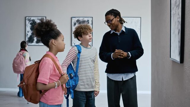 Black male educator explaining modern artwork to diverse children in art gallery. Perfect for educational programs, museum promotions, and school field trip concepts