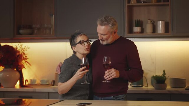 Joyful couple in their 50s enjoy home date, drinking wine and talking at home
