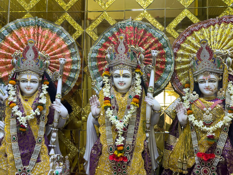 Gilded altar with three ornate statues of Hindu deities adorned with garlands and umbrellas.