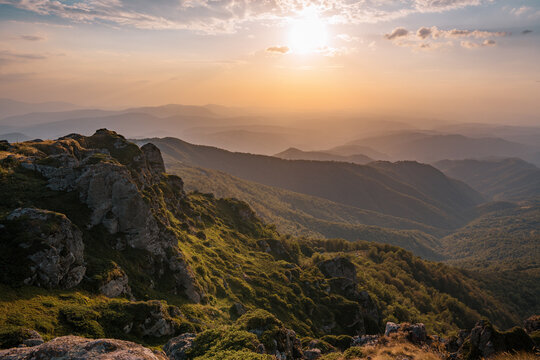 Breath-taking view from Babin Zub rocky peak during golden hour sunset, showing steep cliffs and misty mountain layers stretching to the horizon at Stara Planina mountain, Serbia.