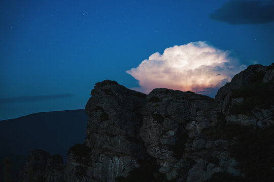 Night atmosphere photo of rocky Babin Zub peaks under a starry sky with a glowing illuminated thunderstorm cloud in the background at Stara Planina mountain, Serbia.