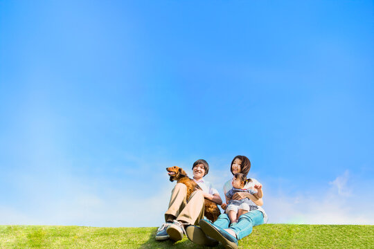 青空を背景に犬のペットと芝に座る幼い女の子と幸せな家族