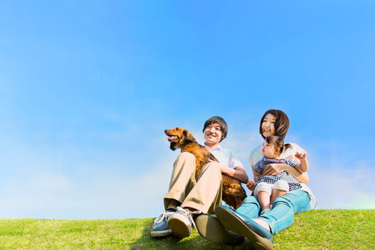 青空を背景に犬のペットと芝に座る幼い女の子と幸せな家族