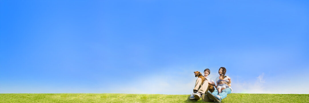 青空を背景に犬のペットと芝に座る幼い女の子と幸せな家族