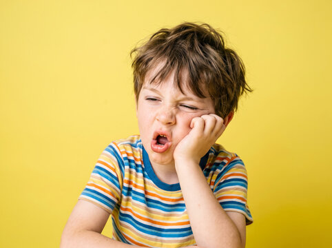Young boy making a ridiculous expression with hand on face on yellow background