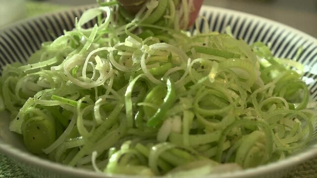 Close up of chef hand mixing fresh sliced green leeks with pepper to prepare a healthy vegetable salad, slow motion.