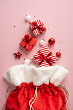 Merry Christmas and Happy New Year flatlay with Santa Claus present, red velvet sack and ornaments on vertical pastel background