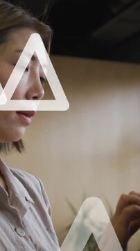 Animation of white triangles moving over asian businesswoman using digital tablet in office