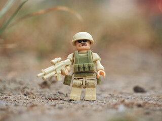 Naklejka premium Indonesia - August 16, 2023 : Mini toy of action figure at outdoor with blurred background. Miniature photography concept design. Minifigure of military army character with bulletproof vest and gun.