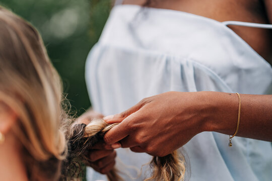 Woman carefully braiding another persons long blonde hair
