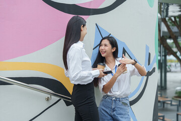 Asian businesswomen chatting with coffee cups in front of colorful mural background © itchaznong