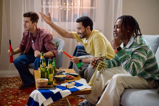 Diverse young adult male football fans watching match at home, cheering and celebrating victory. Image suitable for sports broadcasting, entertainment, and social gathering campaigns