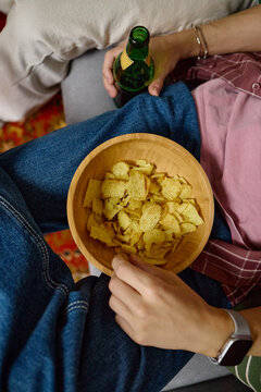 Vertical image of young adult male football fans eating potato chips and holding beer bottle while watching game, perfect for snack food advertising