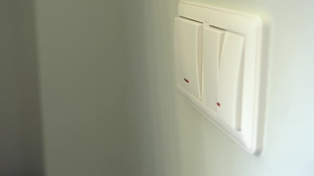 Turning on the electric lights in a room. A woman's hand presses the wall switch.